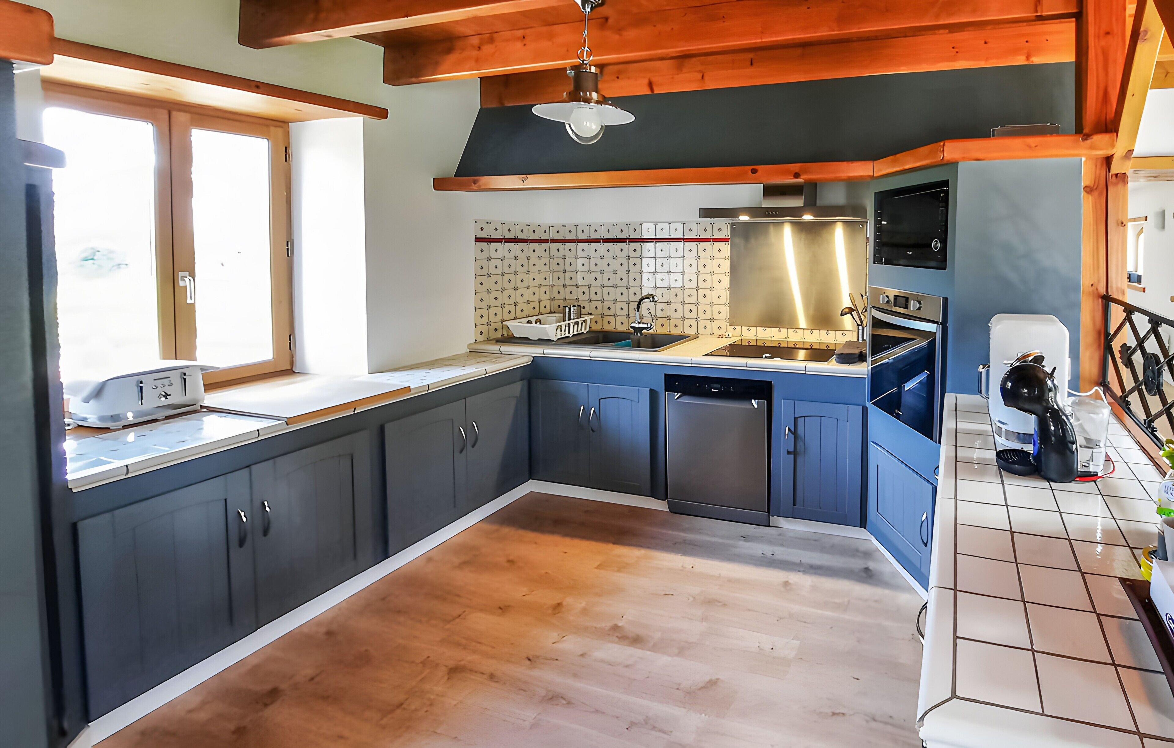 Cocina con vigas de madera, lavavajillas, estufa y ventana.
