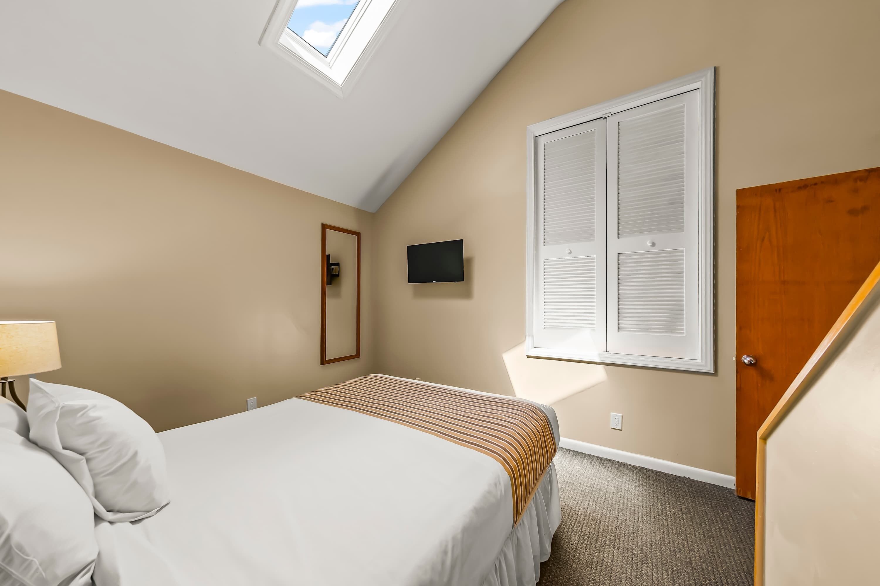 Un dormitorio con cama, televisión, ventana y puerta.