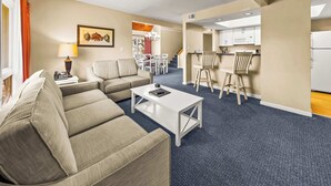 A hotel room with a living area, a dining table, a kitchen, and a staircase. - Family-Friendly Townhome at Sand Castle Village- Pool, Lake & Fun! (New Bern)