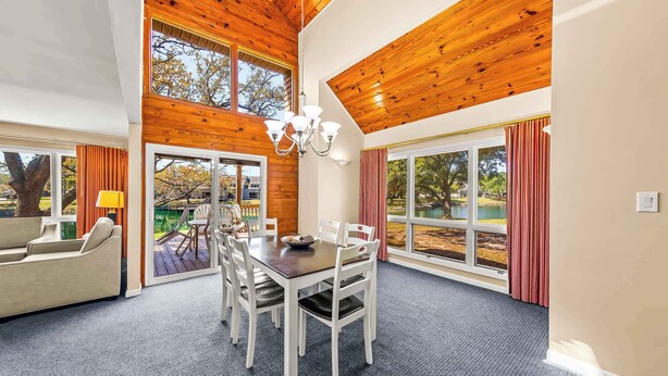 A spacious room with a dining table, white chairs, a chandelier, and large windows offering a view of the outdoors. - Family-Friendly Townhome at Sand Castle Village- Pool, Lake & Fun! (New Bern)