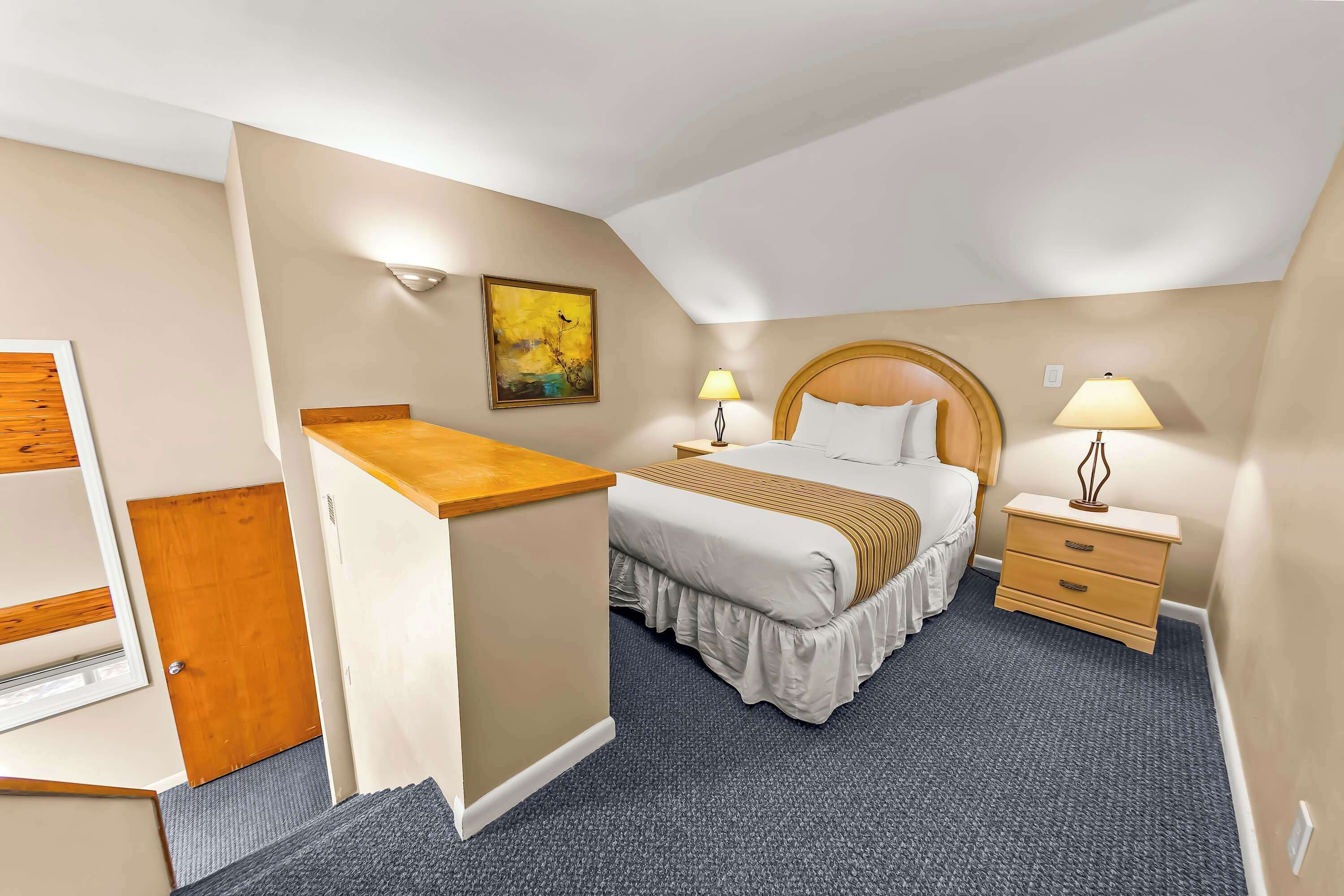 Een hotelkamer met een bed, nachtkastjes, een bureau, een schilderij en een deur.