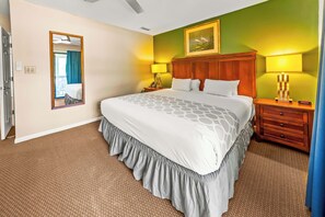 A hotel room with a large bed, two bedside tables, a mirror, and a painting on the wall. - New Bern Condo Getaway: Golf, Pool, and Family-Friendly Comfort! (New Bern)