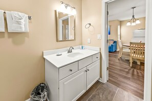 A bathroom with a white sink, mirror, and cabinets. There is a trash bin and a towel rack with towels. - Family Friendly Condo with Golf, Pools & River Access! (New Bern)