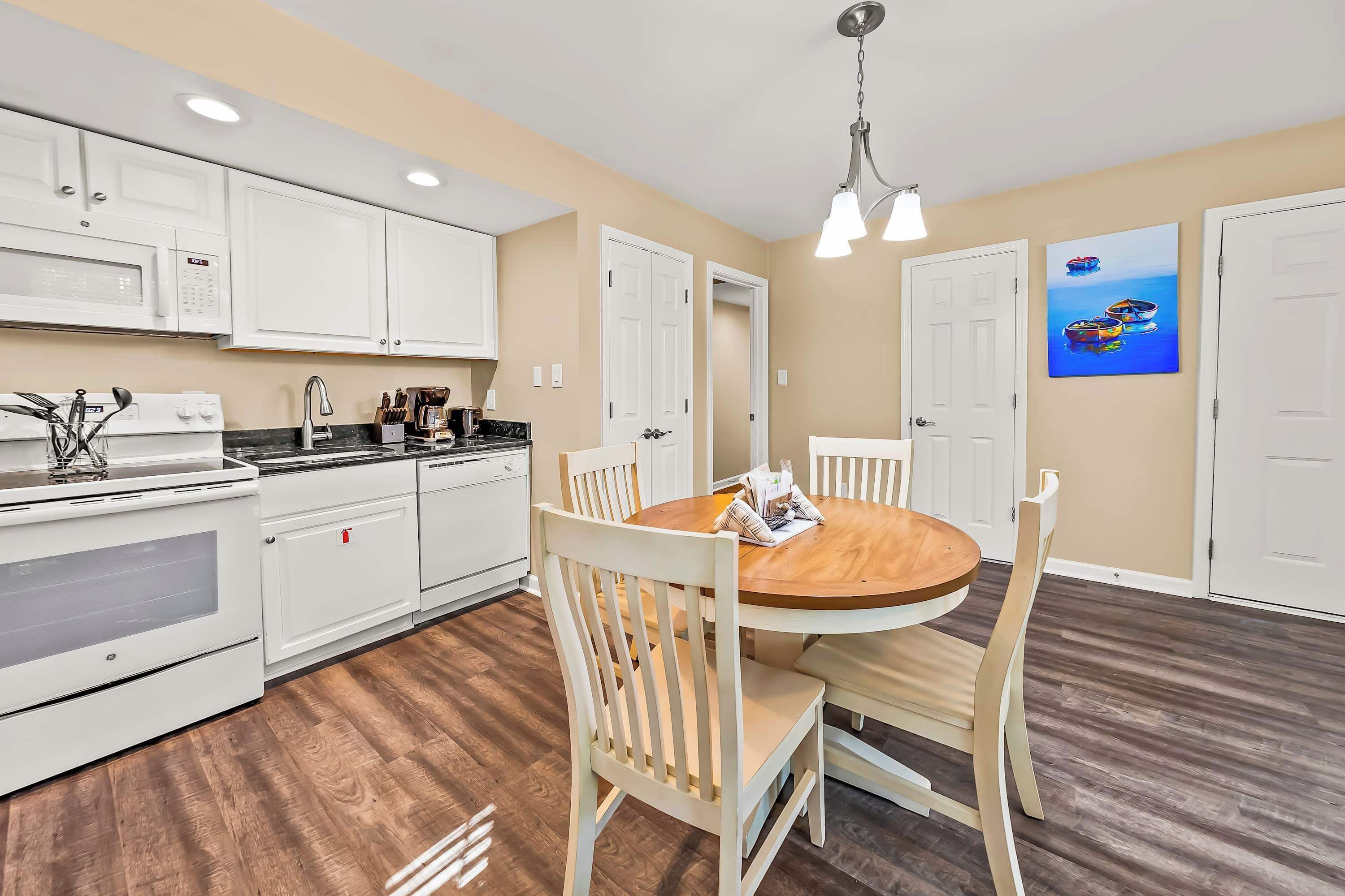 A kitchen with white cabinets, a microwave, a stove, and a dining area with a wooden table and chairs.