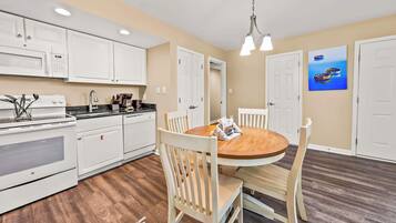 A kitchen with white cabinets, a microwave, a stove, and a dining area with a wooden table and chairs.
