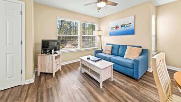 A living room with a blue sofa, wooden coffee table, TV stand, and a ceiling fan.