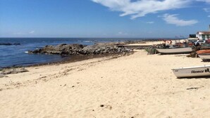 Una playa arenosa con barcos y un rompeolas rocoso.