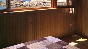 Una habitación con paredes de madera, un ventanal con vistas a una costa rocosa y un suelo a cuadros.