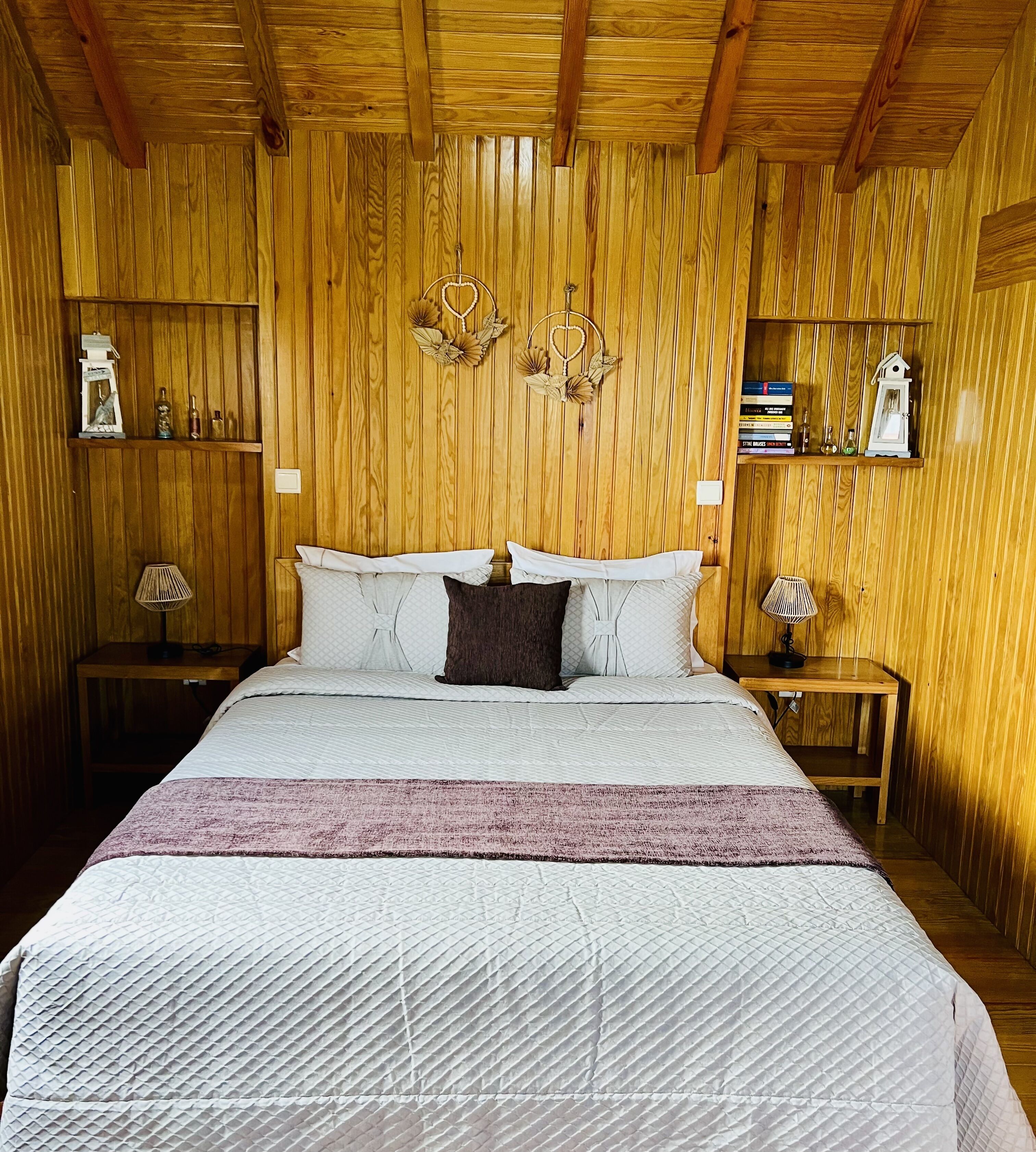 A wooden-paneled bedroom with a bed, bedside lamps, and shelves with books and decorative items.