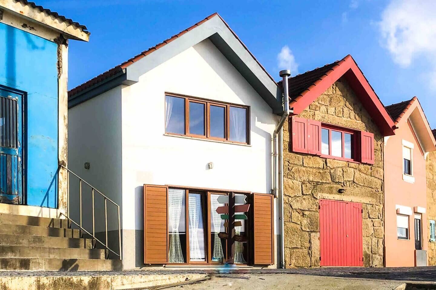 A modern two-story building with a white facade, a red roof, and a stone wall.
