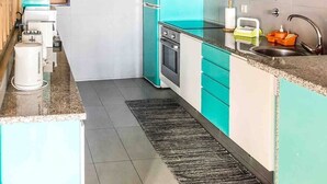 Una cocina compacta con armarios azul turquesa y blancos, un lavamanos de acero inoxidable y un horno empotrado.