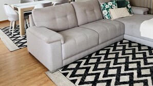 A modern living room with a sectional sofa, a dining table, and a large abstract painting. - Ninho do Carriço - Beach 200m away - Patio & KidsZone (Vila Chã)