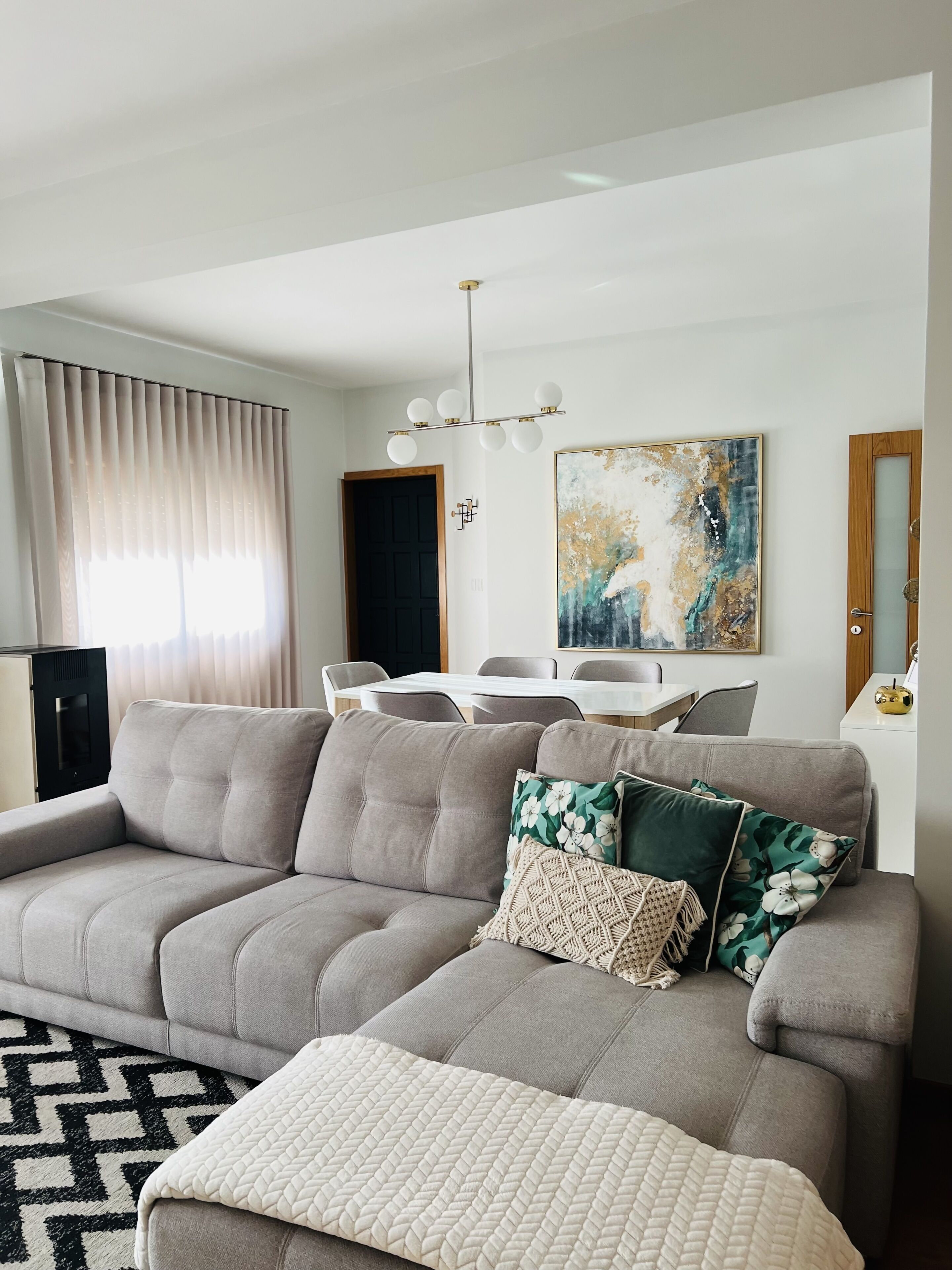 A living room with a grey sofa, a white throw blanket, a dining table with chairs, and a painting on the wall.