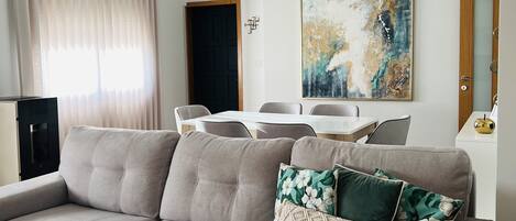 A living room with a grey sofa, a white throw blanket, a dining table with chairs, and a painting on the wall.