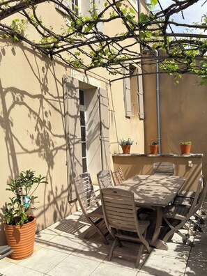 Eine Terrasse mit Tisch, Stühlen, Blumentöpfen und einer Kletterpflanze.