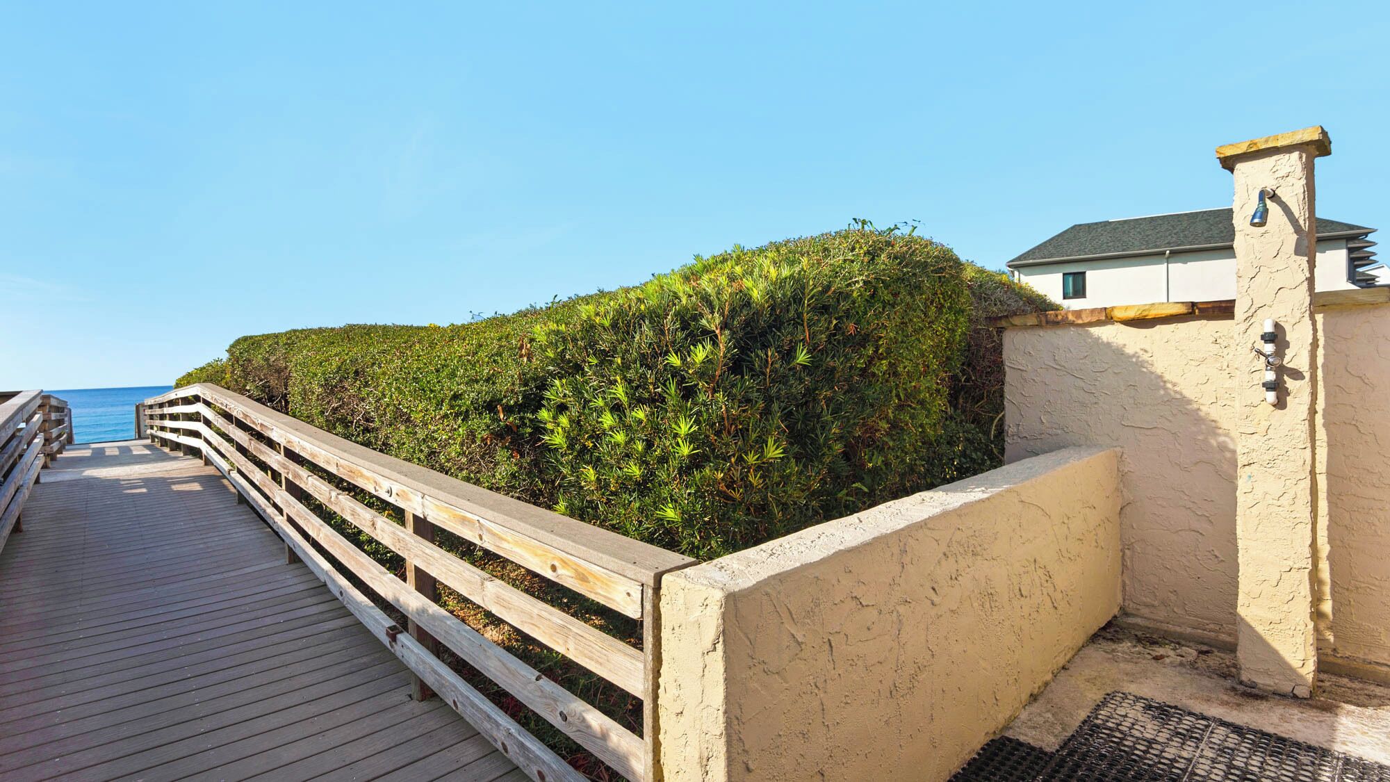 A wooden boardwalk leading to a building with a stone wall and a metal railing.