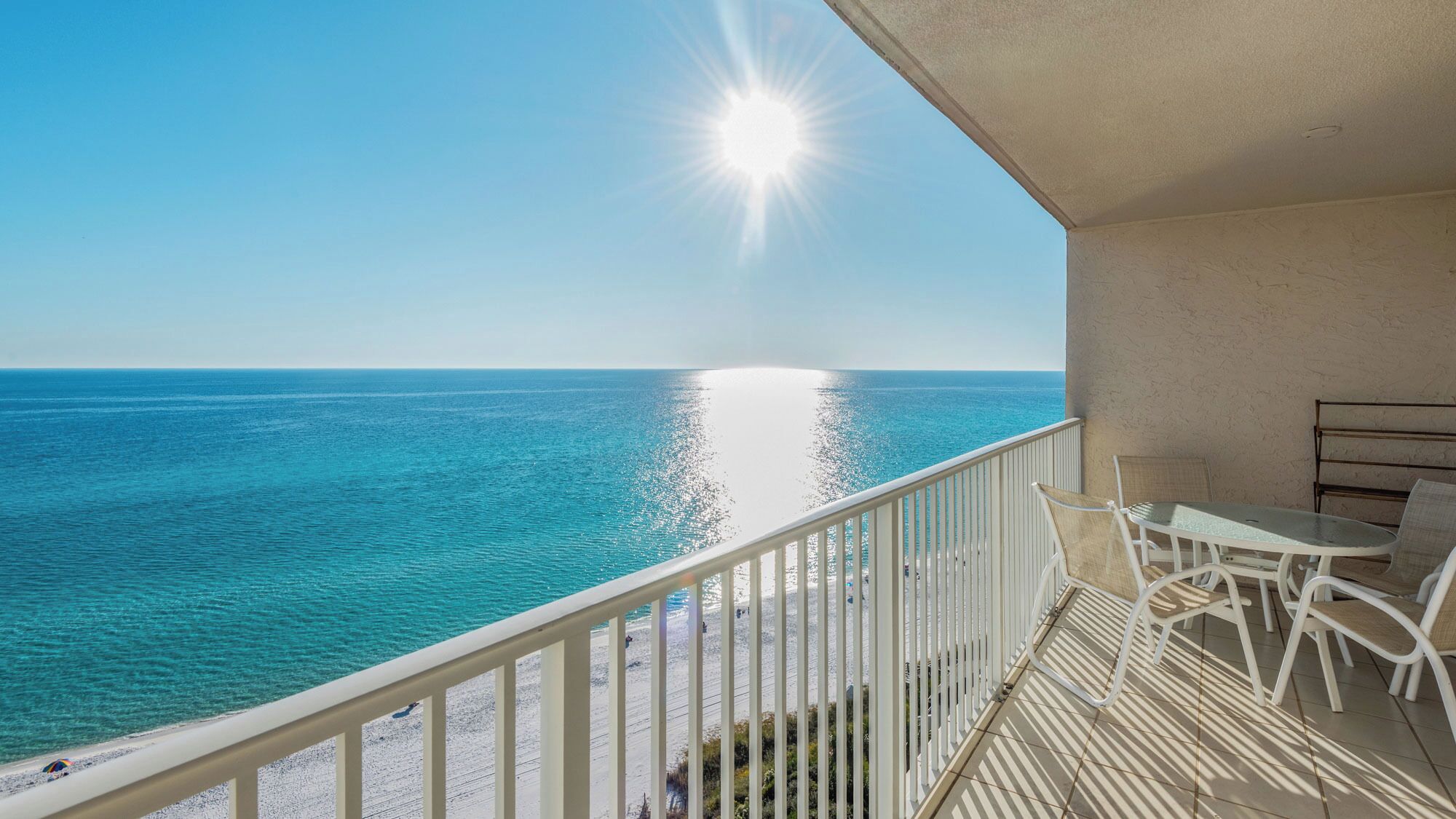 A balcony with a view of the sea, a table, and chairs.