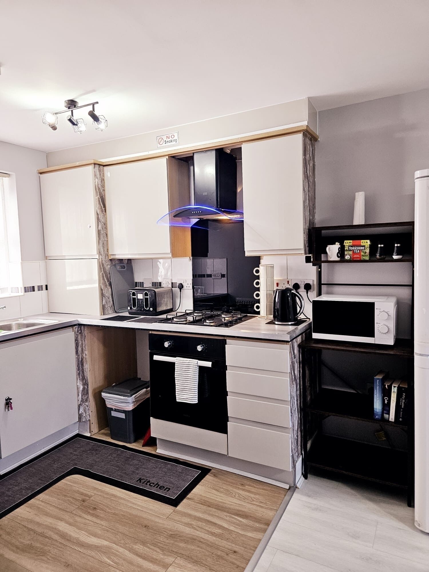 A modern kitchen with white cabinets, a gas stove, a microwave, and a kettle.