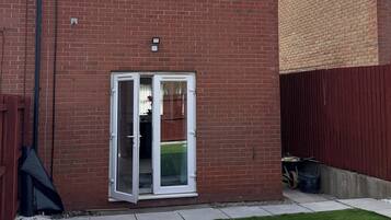 A residential brick house with a front door, two windows, and a small front yard with grass.