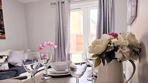 A dining table with white plates, bowls, and glasses, a pitcher, and a vase with flowers. - Modern 2BR 5minutes walk Anfeild| Free parking+ Ev (Liverpool)
