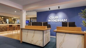 A reception desk with a marble design, a blue wall with 'CLUB WYNDHAM' signage, and a stone wall in the background.