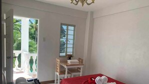 A hotel room with a bed, a table with a chair, a window, and a balcony with a view of greenery. - Las casas resort dingalan (Dingalan)