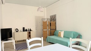 Una sala de estar con televisor, muebles blancos, un sofá azul turquesa y una estructura de cesta tejida.