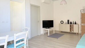 Una sala de estar moderna con una mesa de comedor, sillas, un televisor, un armario y una lámpara colgante.
