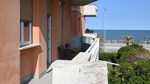 Un balcón con vistas al mar, una mesa con sillas y una pequeña zona ajardinada.