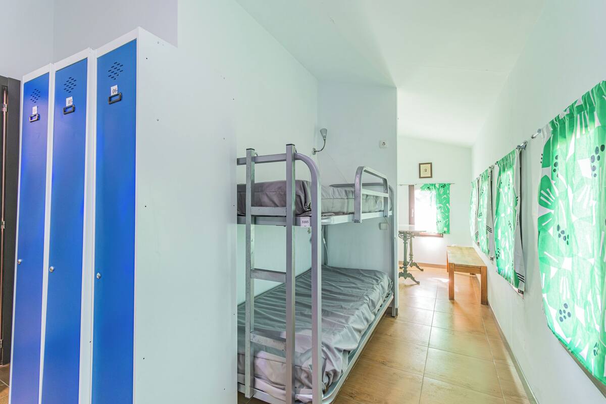 Bunk beds, a bench, and a table in a room with lockers and patterned curtains.