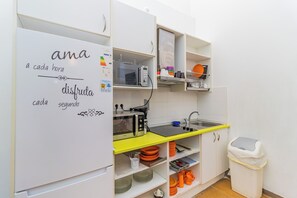 A compact kitchen with a microwave, sink, and shelves containing dishes and utensils.