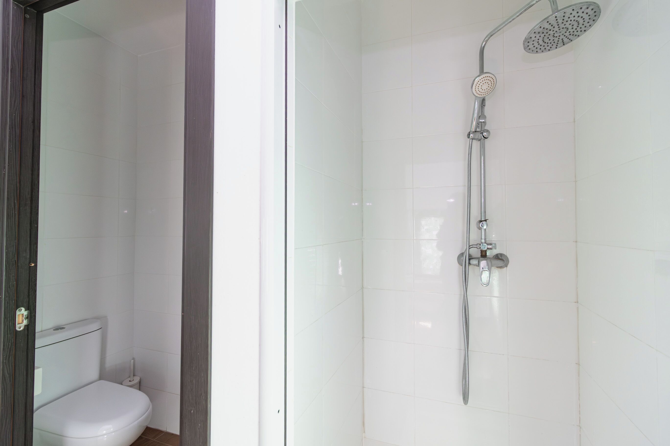 Un baño con inodoro, ducha con cabezal de ducha manual y puerta de vidrio.