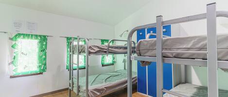 Un dormitorio con literas, una ventana con cortina verde y un armario azul.