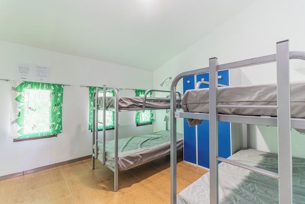 A dormitory room with bunk beds, a window with a green curtain, and a blue locker.