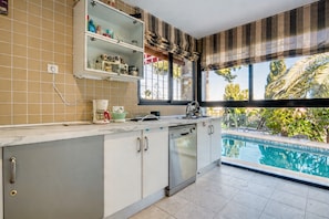 A kitchen with a dishwasher, a coffee maker, and a window with a view of a swimming pool.
