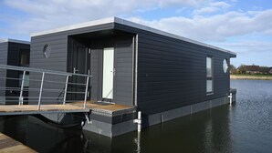 A modern floating house with a dock, large windows, and a flat roof.