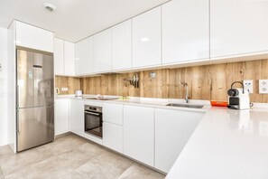 Una cucina moderna con pensili bianchi, un frigorifero in acciaio inossidabile, un forno e uno schienale in legno.