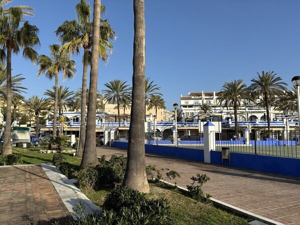 A coastal area with palm trees, a paved walkway, and a blue fence. - Sb3.11g - Modern & Well Connected 2 bed Apartment (Estepona)
