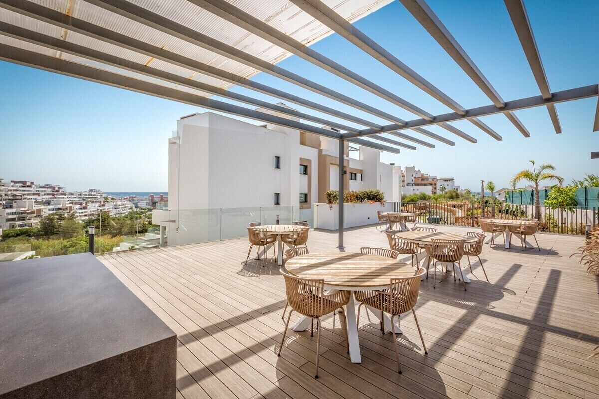 Eine Dachterrasse mit Außenbestuhlung und Blick auf die Stadt, im Hintergrund ein modernes Gebäude.