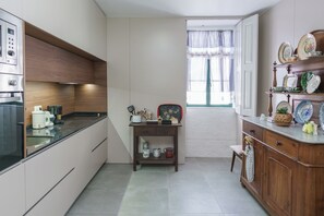 Een moderne keuken met een ingebouwde oven, een koffieapparaat en een houten tafel met keukengerei.
