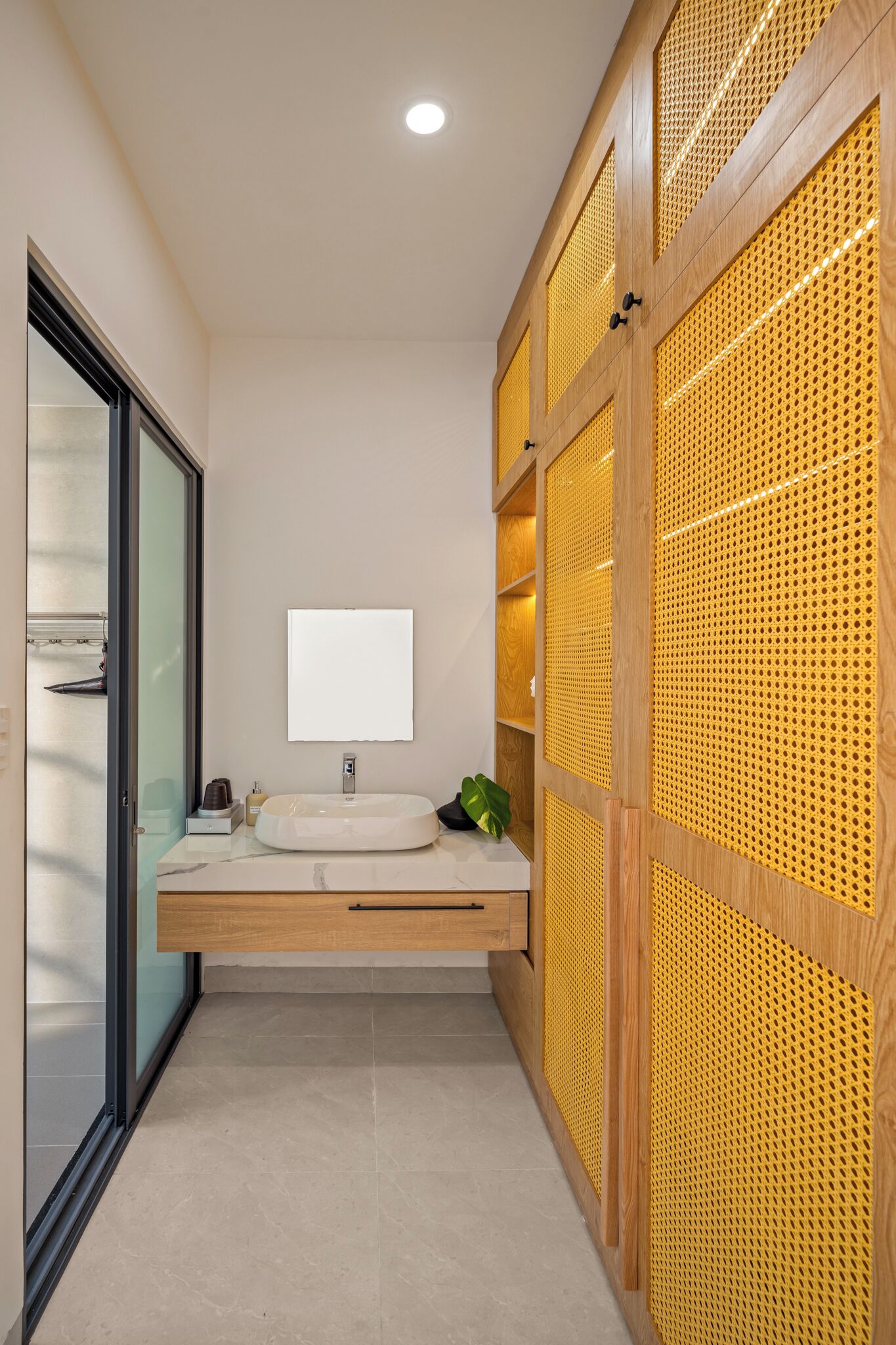 A modern bathroom with a freestanding sink, a mirror, and a wooden storage unit with a perforated design.