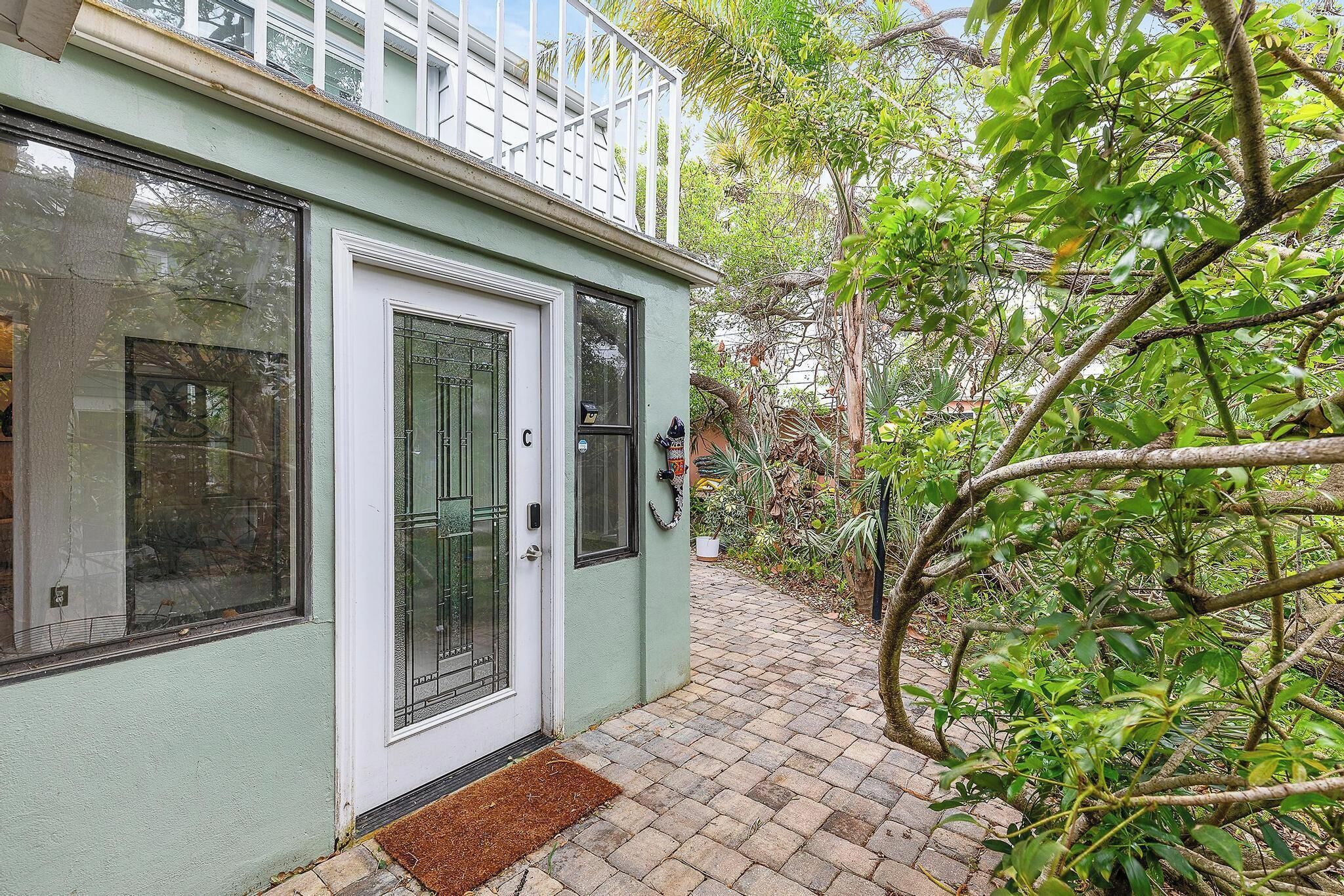 A house with a white door, a small porch, and a garden with trees and plants.