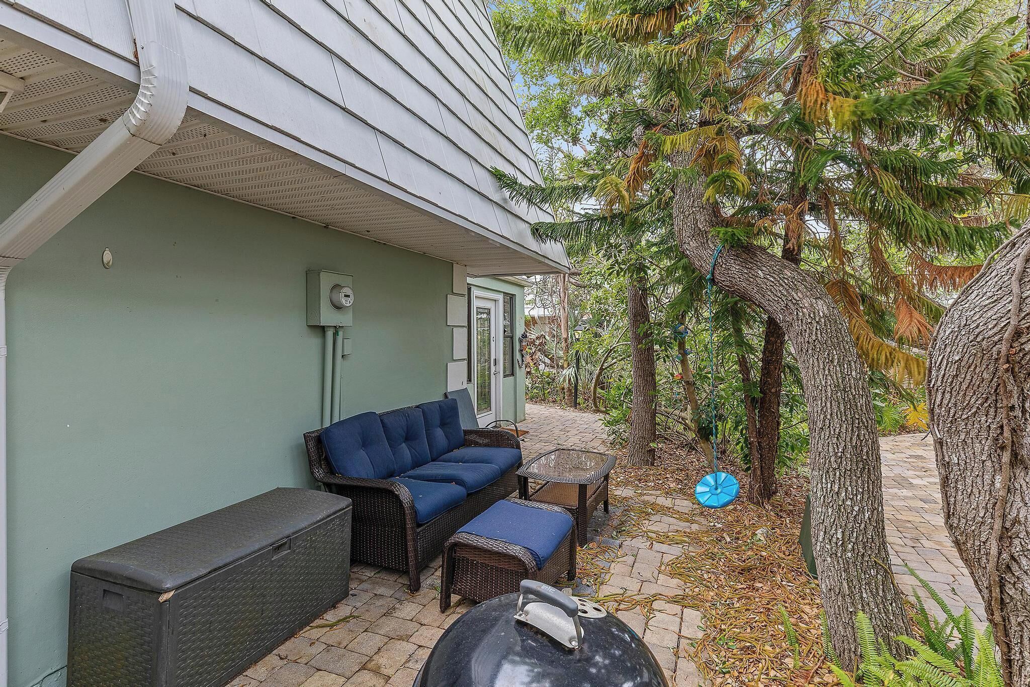 A patio with outdoor furniture, a grill, and a house with a green exterior.
