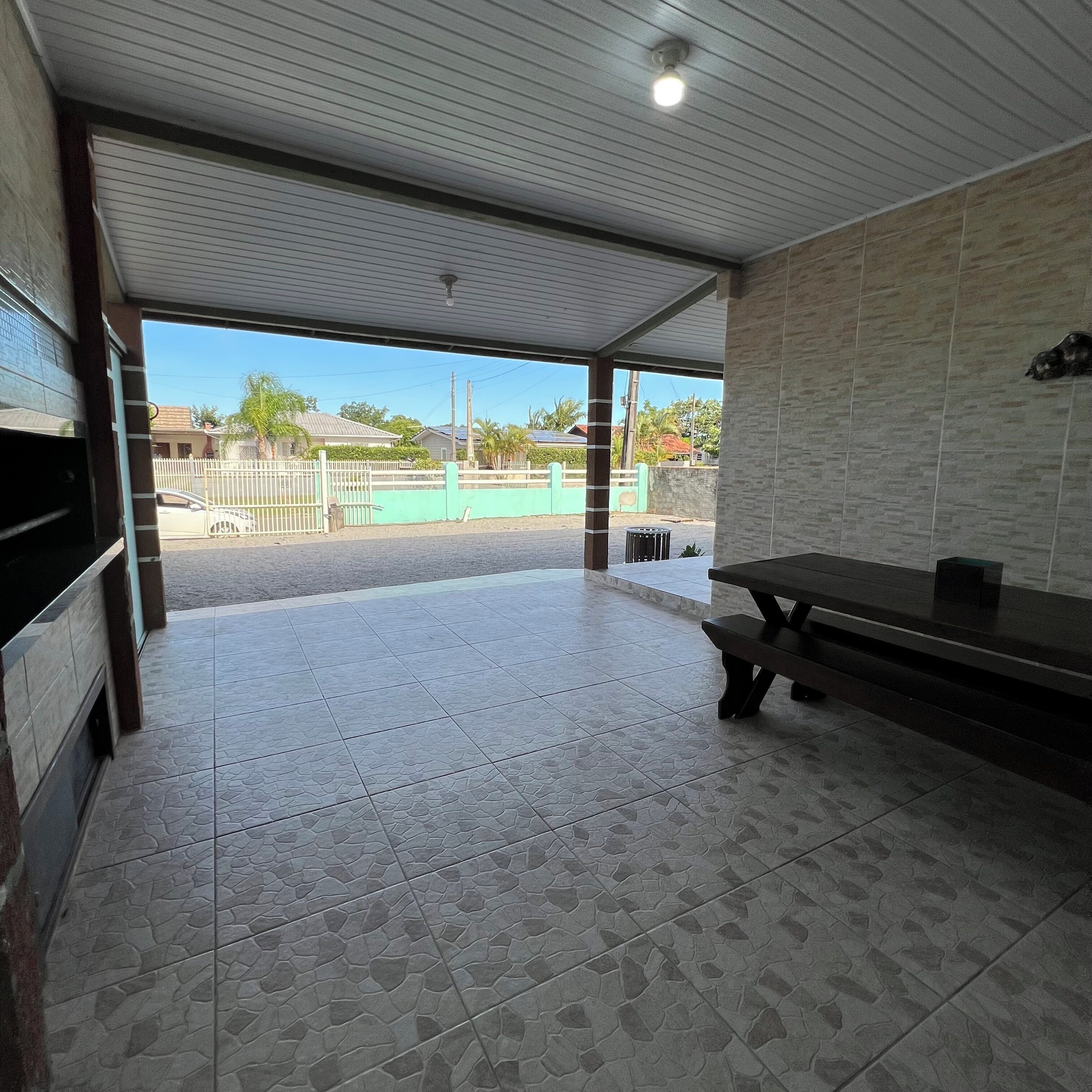 A covered outdoor area with a tiled floor, a bench, and a view of a residential street.