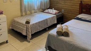 Een hotelkamer met twee eenpersoonsbedden, een houten wand, een raam met gordijnen, een witte dressoir en een airconditioner.
