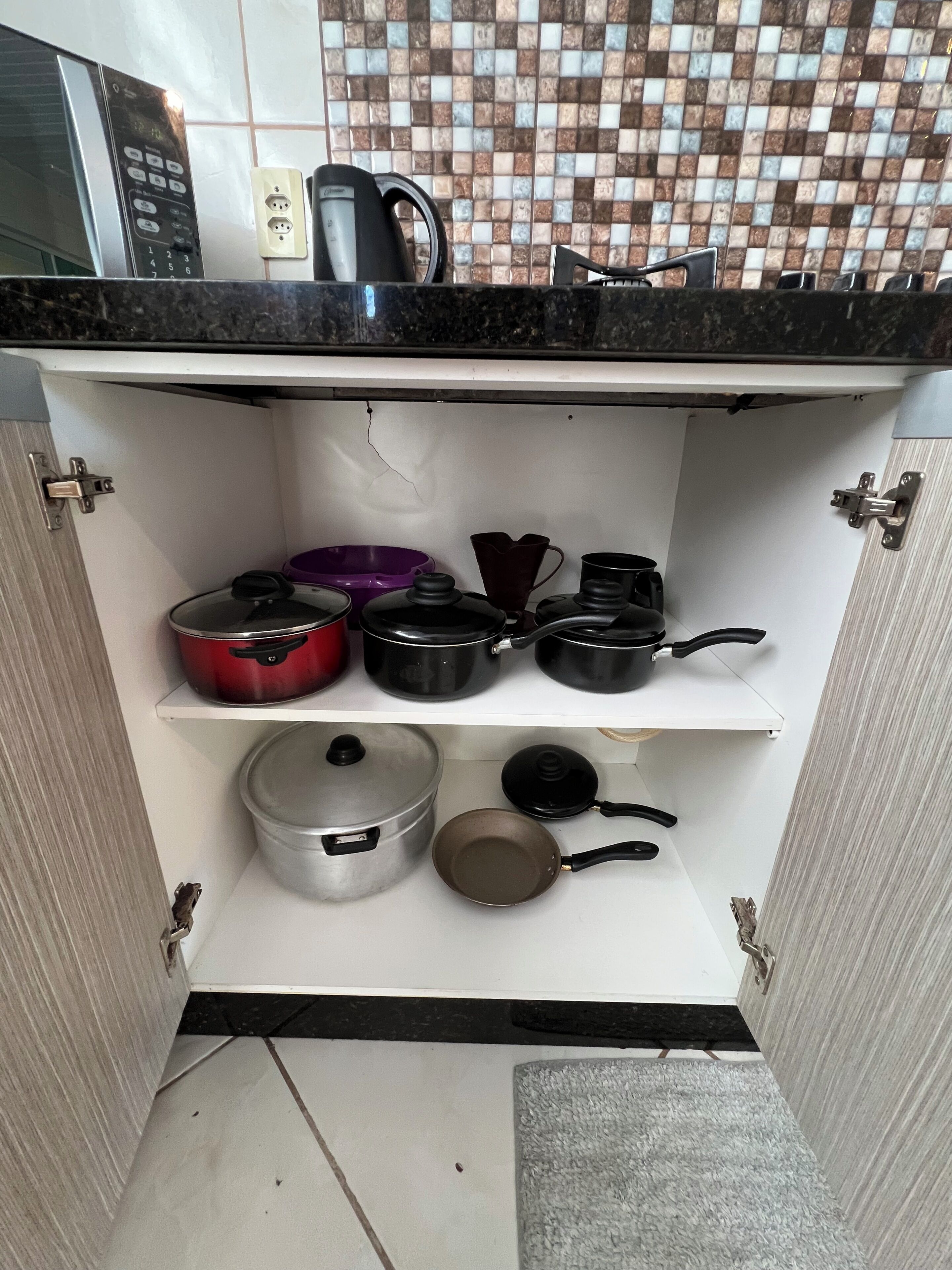 Una cucina con piastrelle a parete, un forno a microonde integrato e diverse pentole e padelle sugli scaffali.