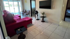 Een woonkamer met een rode bank, een aan de muur bevestigde televisie en een plafondventilator.