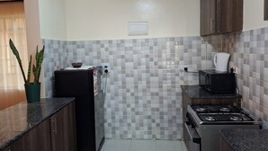 A compact kitchen with a refrigerator, microwave, stove, and tiled backsplash.