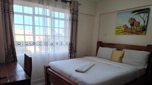 A bedroom with a wooden bed, a dining table, and a window with curtains.