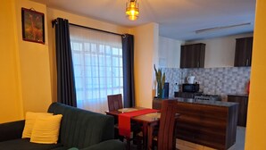 A living room with a sofa, dining table, and kitchen area with cabinets and appliances.